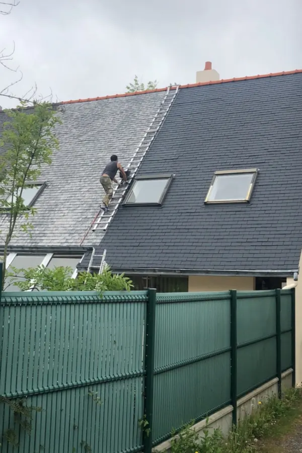 Couvreur sur une toiture en ardoise pendant un chantier d’entretien, échelle en place