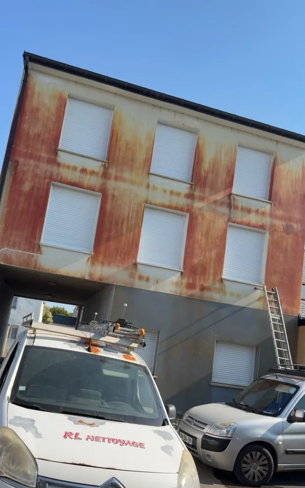 La même façade avant ravalement, couverte de coulures rouges, avec le camion RL Nettoyage devant le chantier