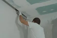 Peintre en bâtiment enduisant un plafond avant peinture intérieure